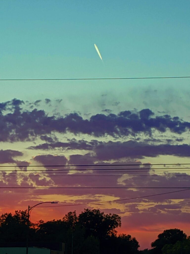 Sunset at Downtown Stillwater Oktoberfest. Beautiful pink, purple and glowing orange clouds at the horizon line that fade into the turquoise blue sky above where a jets looks like it is blasting towards outer space like a comet.